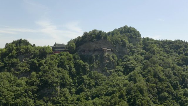 Wudangshan, hanging temple on dense tropical green Jinding mountain. Aerial push in towards magnificent religious destination.