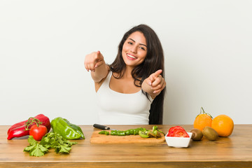 Young curvy woman preparing a healthy meal cheerful smiles pointing to front.