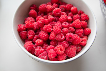 Fresh ripe raspberries in a gray bowl on a white table.