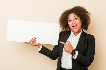 Young african american woman holding a placard smiling cheerfully pointing with forefinger away.