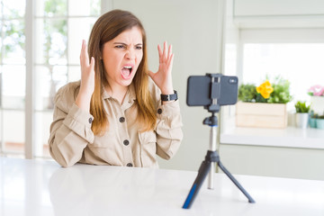 Fototapeta premium Beautiful young woman doing online video call using smartphone webcam celebrating mad and crazy for success with arms raised and closed eyes screaming excited. Winner concept