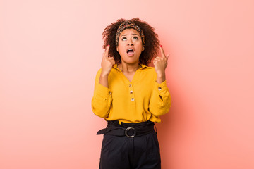 Young african american woman against a pink background pointing upside with opened mouth.