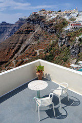 White balcony and table with two chairs overlooking windy steps from harbour and clifftop town of Thira, Santorini, Greek Islands