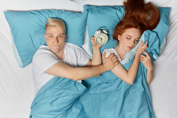 frustrated nervous sleepy man cannot turn off alarm clock, asking girlfriend to help him. close up top view photo