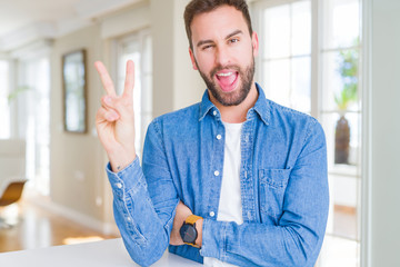 Handsome man at home smiling with happy face winking at the camera doing victory sign. Number two.