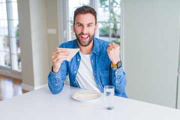 Handsome man eating healthy sandwich screaming proud and celebrating victory and success very excited, cheering emotion