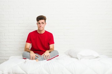 Young teenager student man on the bed confused, feels doubtful and unsure.