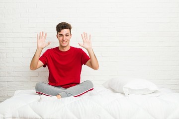 Young teenager student man on the bed showing number ten with hands.