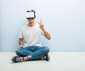 Teenager caucasian man using a virtual reality glasses sitting on the floor