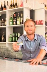 Portrait of smiling young waiter giving change while standing at counter in restaurant