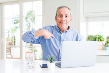 Handsome senior man using computer laptop working on internet with surprise face pointing finger to himself