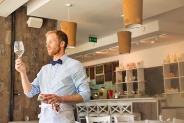 Young waiter looking at empty wineglass in restaurant