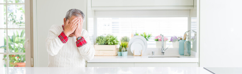 Wide angle perspective of handsome senior man at home with sad expression covering face with hands...