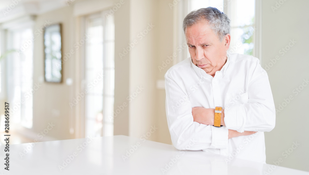 Sticker Handsome senior man at home skeptic and nervous, disapproving expression on face with crossed arms. Negative person.