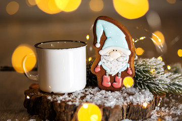 Holiday traditional food bakery. Gingerbread little fairytale gnome in cozy decoration with garland lights and cup of hot coffee