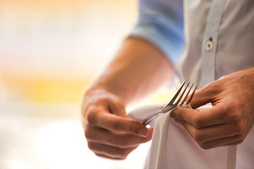Midsection of young waiter cleaning fork in restaurant