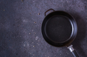 Frying pan and eggs. Empty cast iron pan, eggs, salt, pepper, oil and parsley on black background for cooking fried eggs.