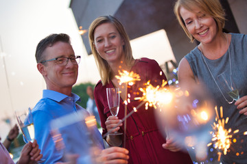 Smiling business colleagues holding sparklers during party on rooftop