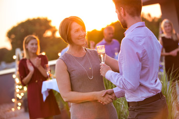 Young businessman shaking hands with mature businesswoman during rooftop party