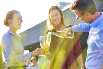 Businessman pouring wine from bottle for smiling businesswomen during success party