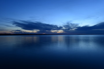 Fototapeta premium blue sky in the twilight glow from behind clouds over the azure calm surface of the water