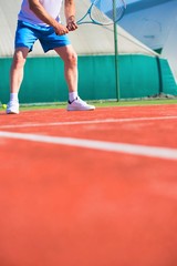 Fototapeta premium Confident mature man hitting tennis ball with racket on red court
