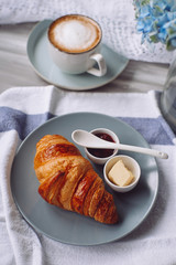 Croissant on a gray plate with butter and jam and a cup of coffee on the table