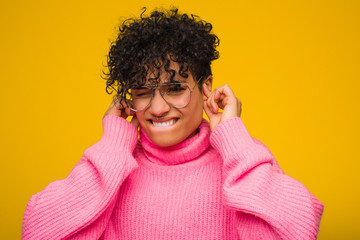 Young african american woman wearing a pink sweater covering ears with hands.