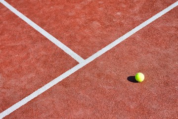 Tennis ball on red court during sunny day