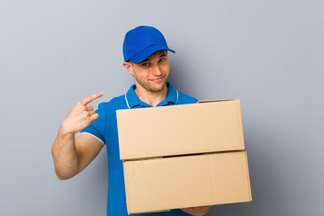 Young man delivering packages pointing with finger at you as if inviting come closer.
