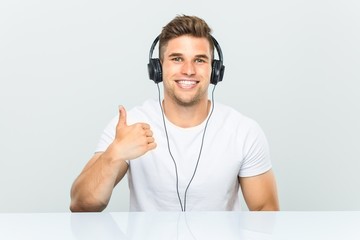 Young man listening to music with headphones smiling and raising thumb up