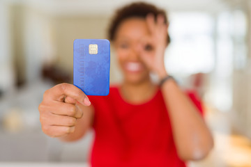 Young african american woman holding credit card with happy face smiling doing ok sign with hand on eye looking through fingers