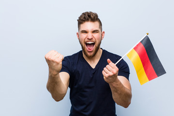 Young caucasian man holding a germany flag cheering carefree and excited. Victory concept.