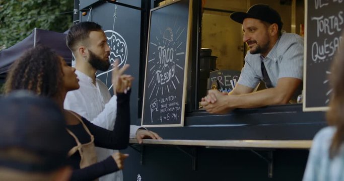 Cheerful waiter taking order from multi-racial customers at counter, Mexican street food served from a food truck. 4K UHD RAW graded footage
