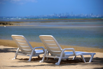 Two white chairs standing on the beach in front the  sea.