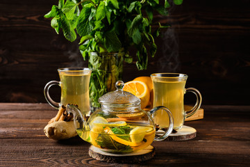 Hot tea with lemon, orange, ginger and mint on rustic wooden table in the morning