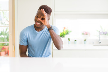 Handsome african american man wearing casual t-shirt at home doing ok gesture with hand smiling, eye looking through fingers with happy face.