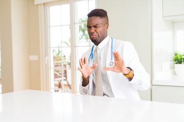 African american doctor man at the clinic disgusted expression, displeased and fearful doing disgust face because aversion reaction. With hands raised. Annoying concept.