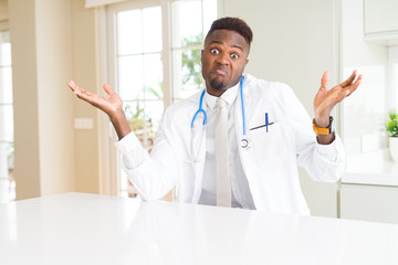 African american doctor man at the clinic clueless and confused expression with arms and hands...