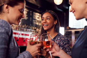 Three Women Making A Toast As They Meet For Drinks And Socialize In Bar After Work