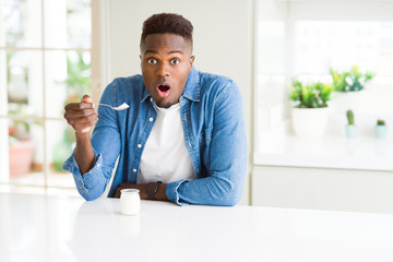 African american man eating healthy natural yogurt with a spoon scared in shock with a surprise face, afraid and excited with fear expression