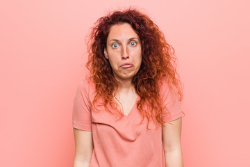 Young natural and authentic redhead woman shrugs shoulders and open eyes confused.