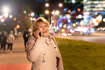 A woman with a mobile phone in her hand is walking through the night city.