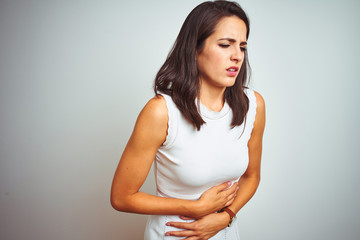 Young beautiful woman wearing dress standing over white isolated background with hand on stomach because indigestion, painful illness feeling unwell. Ache concept.