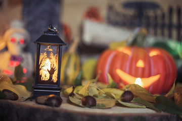 Halloween decorations concept at night. Close up of jack o'lantern, vintage lanterns, pumpkins, skull, autumn leaves. Colorful halloween lights on evening. Happy Halloween scene on wooden background