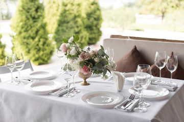 Wedding table setting decorated with fresh flowers in a brass vase. Wedding floristry. Banquet table for guests outdoors with a view of green nature. Bouquet with roses, eustoma and eucalyptus leaves