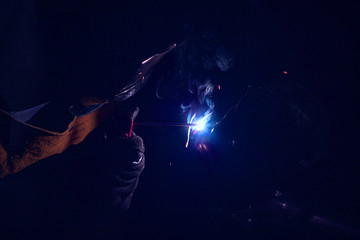 Naklejka premium A welder at work. Sparks flying. Welder in mask at work. Profession of a welder. Sparks around. Welding metal. Dark background.