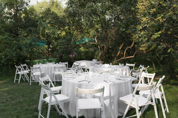 Wedding table setting decorated with fresh flowers in a brass vase. Wedding floristry. Banquet table for guests outdoors with a view of green nature. Bouquet with roses, eustoma and eucalyptus leaves