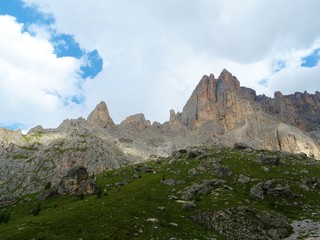 Fototapeta na wymiar The peaks of the Dolomites of the Sassolungo Massif immersed in the clouds and in the nature of Trentino - Alto - Adige, Near the town of Canazei, Italy - August 2019.