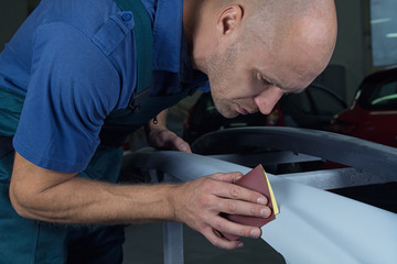 A man who sanding with a grinder and prepares the paint for the car in a car service. Repairman fix car paint.